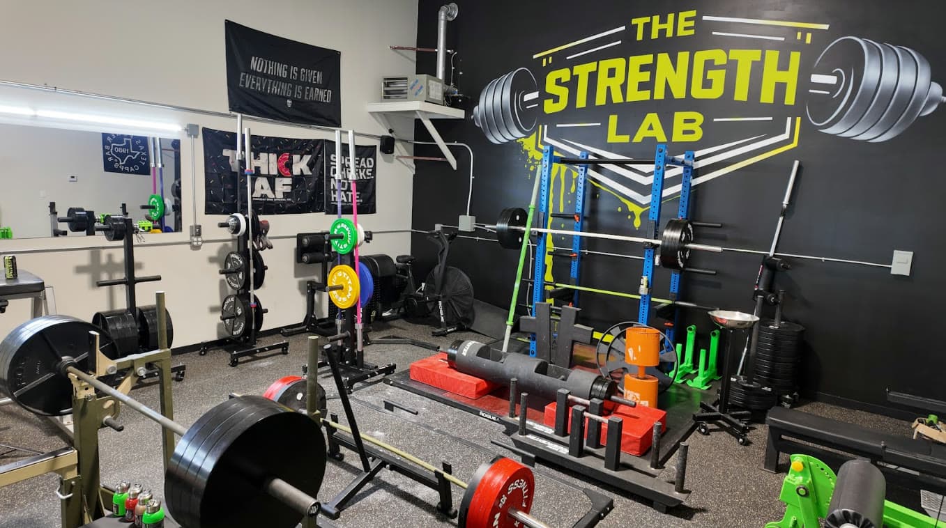 Wide view of The Strength Lab floor: squat racks, plate trees, kilo plates, deadlift platforms and the branded wall mural