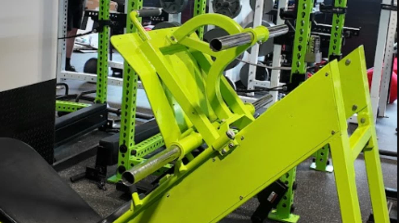 Green plate-loaded leg press with an extra-wide footplate in front of the power racks